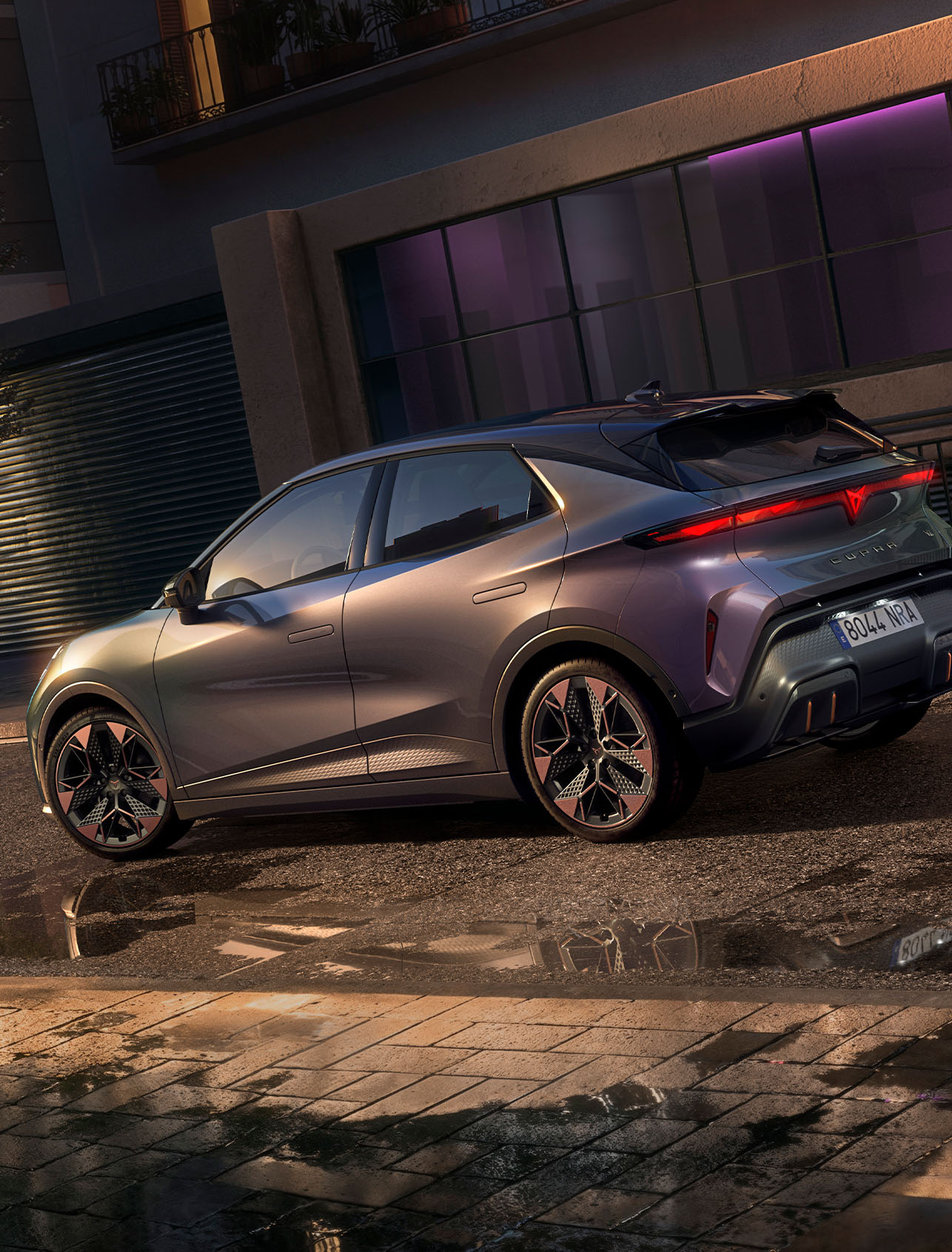 Close-up van de achterzijde van de CUPRA Raval VZ in Plasma met 19 inch lichtmetalen velgen, geparkeerd in een stedelijke straat bij nacht.