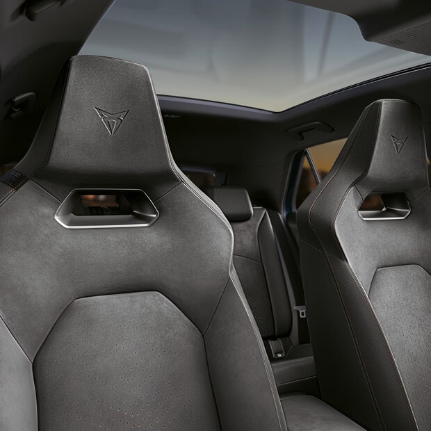 Een close-up van het interieur van een CUPRA auto, met de nadruk op de hoofdsteun en het bovenste gedeelte van een CUPRA Bucket seat in donker suède, met daarin het CUPRA logo in reliëf en een panoramisch zonnedak erboven.