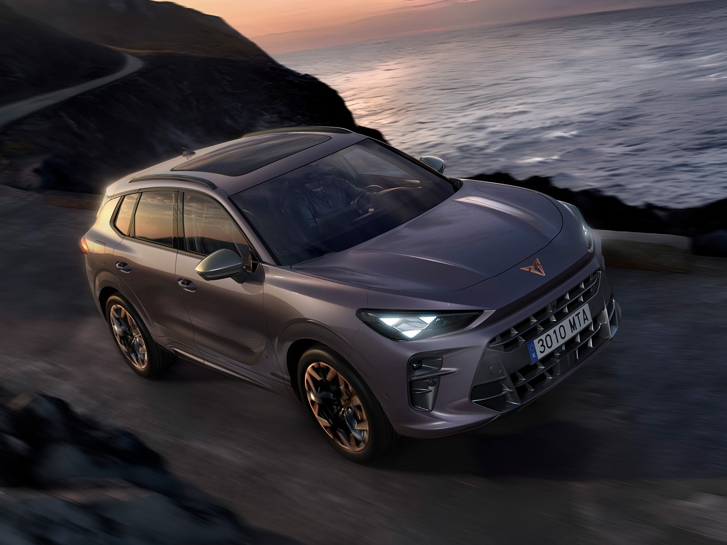 CUPRA Terramar met Dynamic Chassis Control (DCC), rijdend over een kustweg, uitgevoerd in Dark Void-lak en voorzien van 20 inch Hadron Copper lichtmetalen velgen.