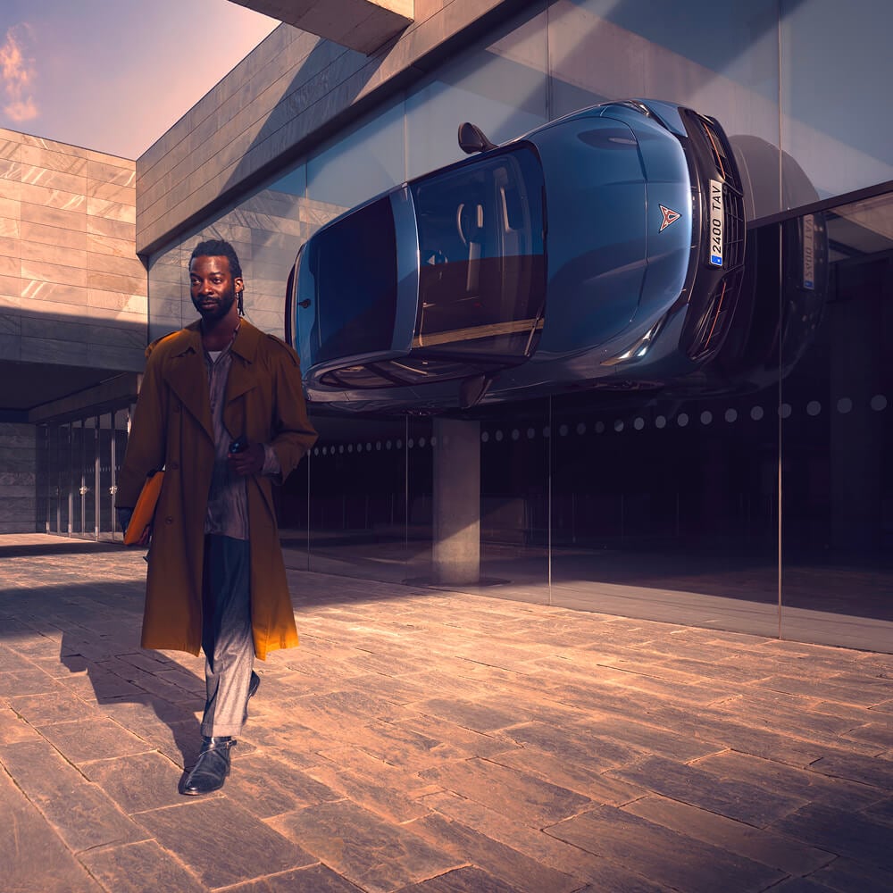 Man loopt weg van een geparkeerde CUPRA Tavacan op de zijkant van een kantoorgebouw